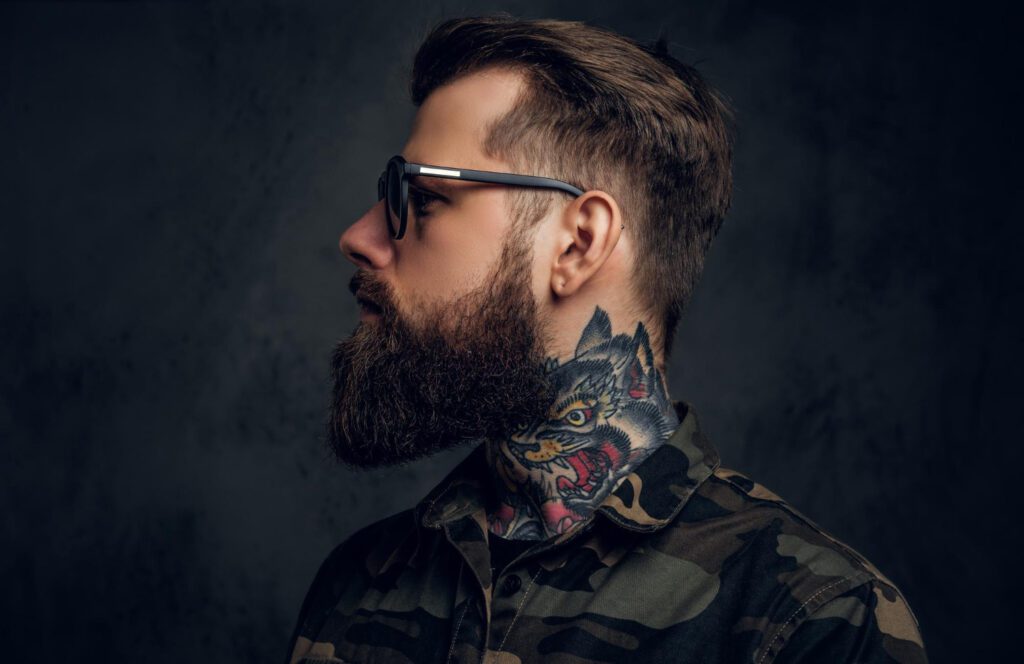 closeup profile bearded man with tattoo his neck sunglasses wearing military shirt studio photo against dark wall